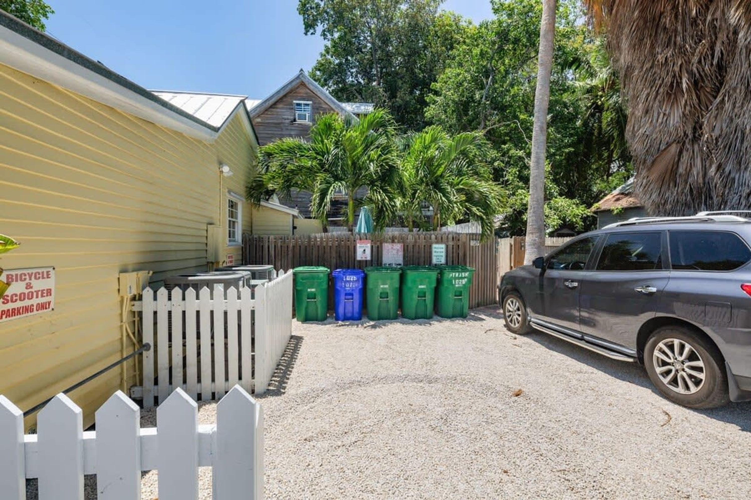 A gated parking area with a bicycle and scooter sign, a car, and recycling bins.
