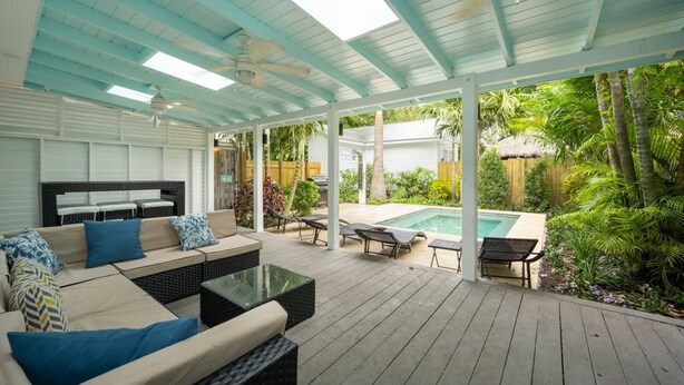 A covered outdoor patio with a pool, seating area, and lush greenery. - Coconut Palm by Brightwild Island Home w Pool (Key West)