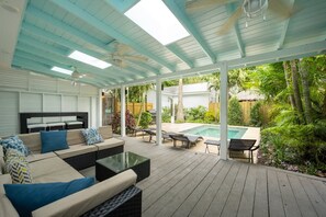A covered outdoor patio with a pool, seating area, and lush greenery. - Coconut Palm by Brightwild Island Home w Pool (Key West)