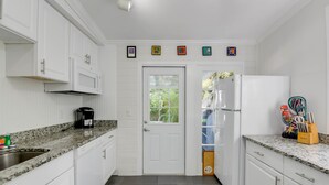 A kitchen with white cabinets, a granite countertop, a coffee maker, and a refrigerator. - Coconut Palm by Brightwild Island Home w Pool (Key West)