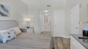 A bedroom with a bed, bedside table, lamp, and a painting on the wall. - Coastal Condo 607 by Brightwild Beachfront (Panama City Beach)