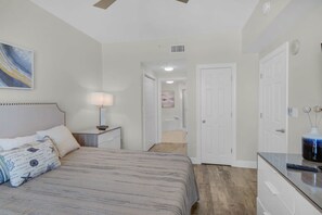 A bedroom with a bed, bedside table, lamp, and a painting on the wall. - Coastal Condo 607 by Brightwild Beachfront (Panama City Beach)