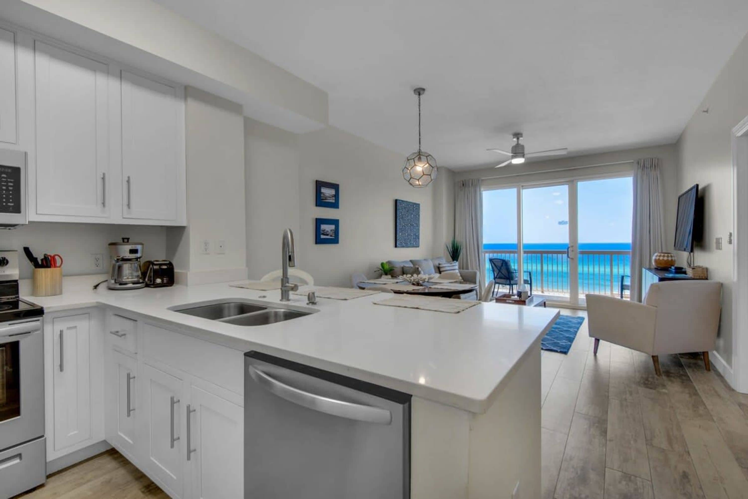 A modern kitchen with white cabinetry, a large island with a sink, and a view of the ocean through the sliding glass doors.