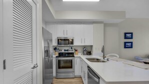 A modern kitchen with white cabinets, stainless steel appliances, and a large island with a sink. - Coastal Condo 607 by Brightwild Beachfront (Panama City Beach)