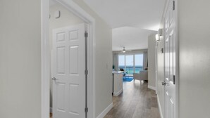 A hallway with a white door, a view of a balcony with a blue sky, and a ceiling fan. - Coastal Condo 607 by Brightwild Beachfront (Panama City Beach)