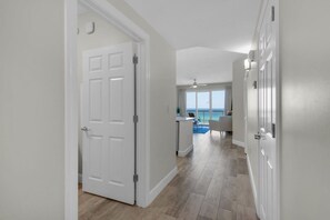 A hallway with a white door, a view of a balcony with a blue sky, and a ceiling fan. - Coastal Condo 607 by Brightwild Beachfront (Panama City Beach)