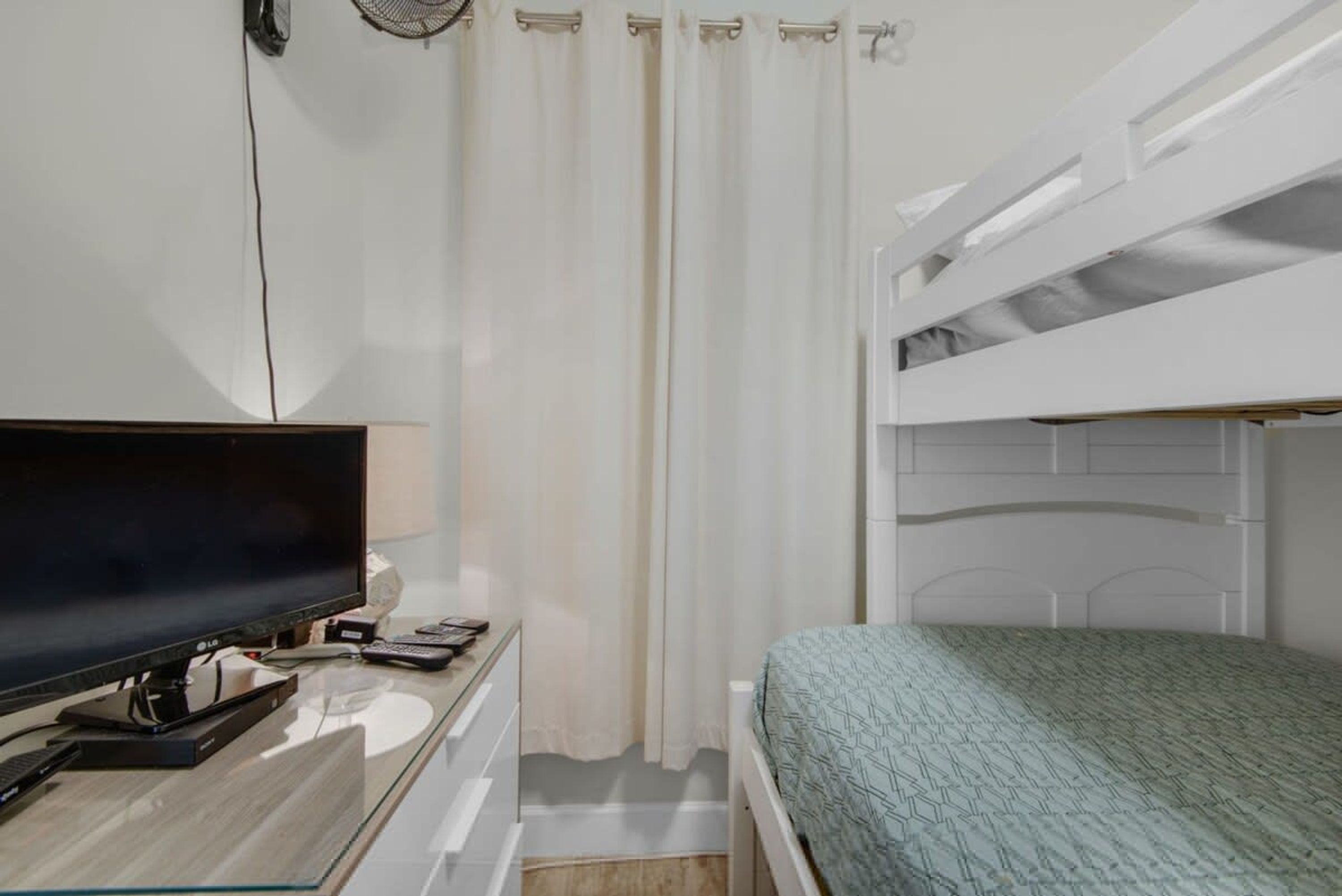 A bedroom with a bunk bed, a desk with a flat-screen TV, and a curtain.