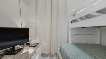 A bedroom with a bunk bed, a desk with a flat-screen TV, and a curtain.