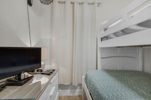 A bedroom with a bunk bed, a desk with a flat-screen TV, and a curtain. - Coastal Condo 607 by Brightwild Beachfront (Panama City Beach)