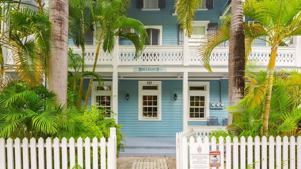 A two-story building with a blue facade, a white picket fence, and palm trees. - Sky Loft by Brightwild Penthouse in Prime Spot (Key West)