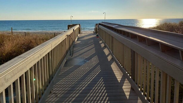 A wooden boardwalk leading to the beach with a clear view of the ocean and the sun setting in the background. - Coastal Condo 807 by Brightwild Beachfront (Panama City Beach)