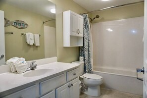 Une salle de bain équipée d’un lavabo, d’un miroir, d’un porte-serviettes, de toilettes et d’un rideau de douche.