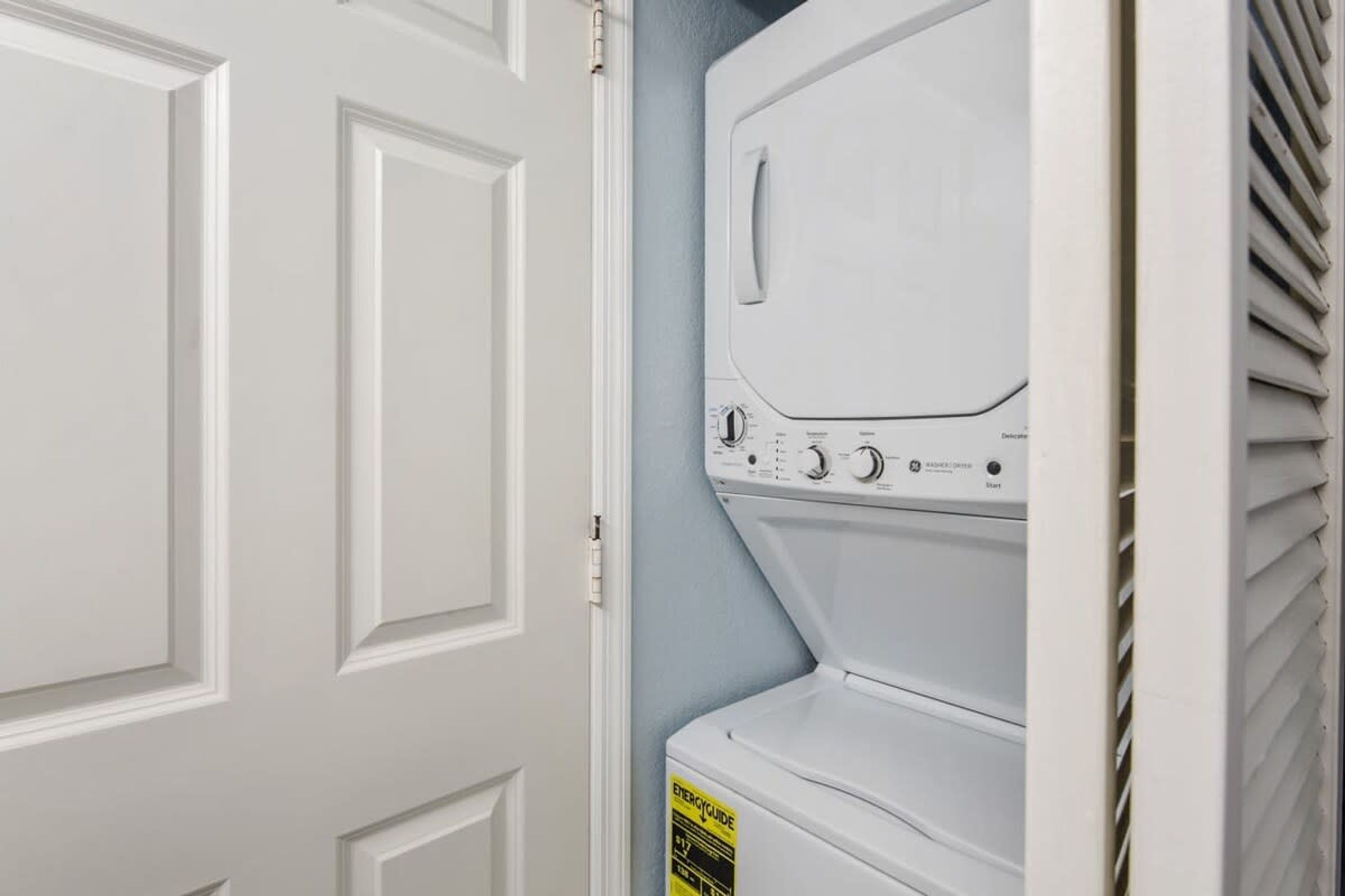 A white wall-mounted washer and dryer unit with a control panel and a yellow energy efficiency label.