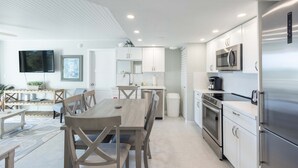A modern kitchen with white cabinets, stainless steel appliances, and a dining area with wooden furniture. - The Exuma Cay by Brightwild Pool View Parking (Key West)