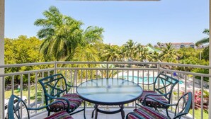 A balcony with a glass table and chairs, overlooking a pool and lush greenery. - The Exuma Cay by Brightwild Pool View Parking (Key West)
