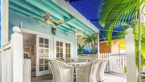 A covered outdoor area with a table and chairs, a ceiling fan, and a mural on the wall. - Gulf Getaway by Brightwild Condo w Pool (Key West)