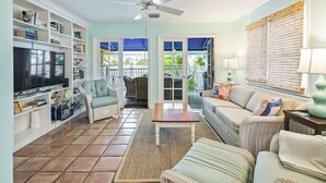 A living room with a television, bookshelves, a sofa, and a ceiling fan. - Gulf Getaway by Brightwild Condo w Pool (Key West)
