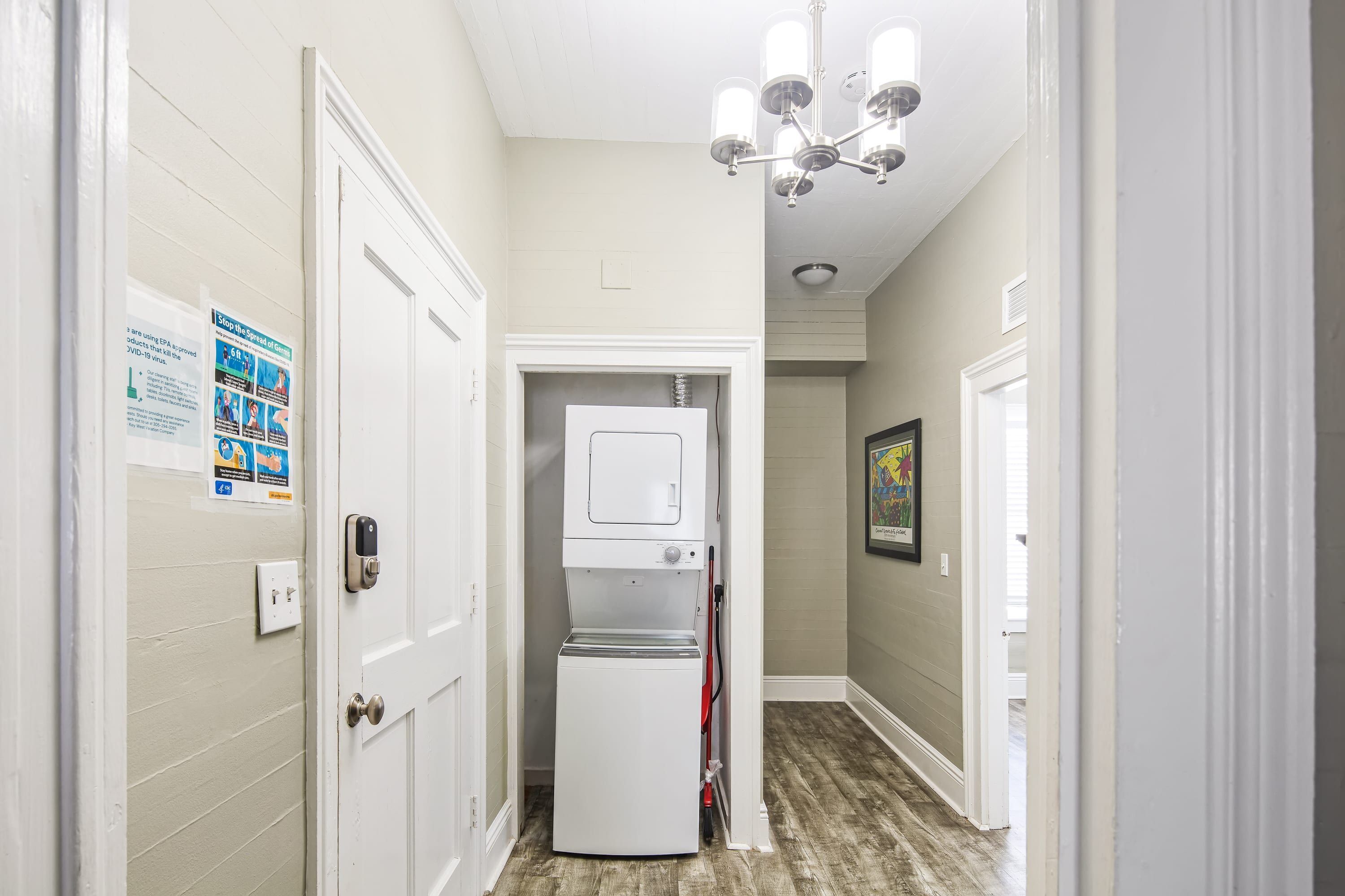A narrow hallway with a laundry machine, a door with a lock, and a chandelier.