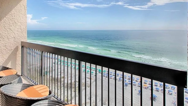 Ein Balkon mit Korbmöbeln mit Blick auf einen Strand mit Sonnenschirmen.