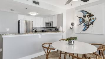 A modern kitchen with white cabinets, stainless steel appliances, a white dining table with wicker chairs, and a ceiling fan.