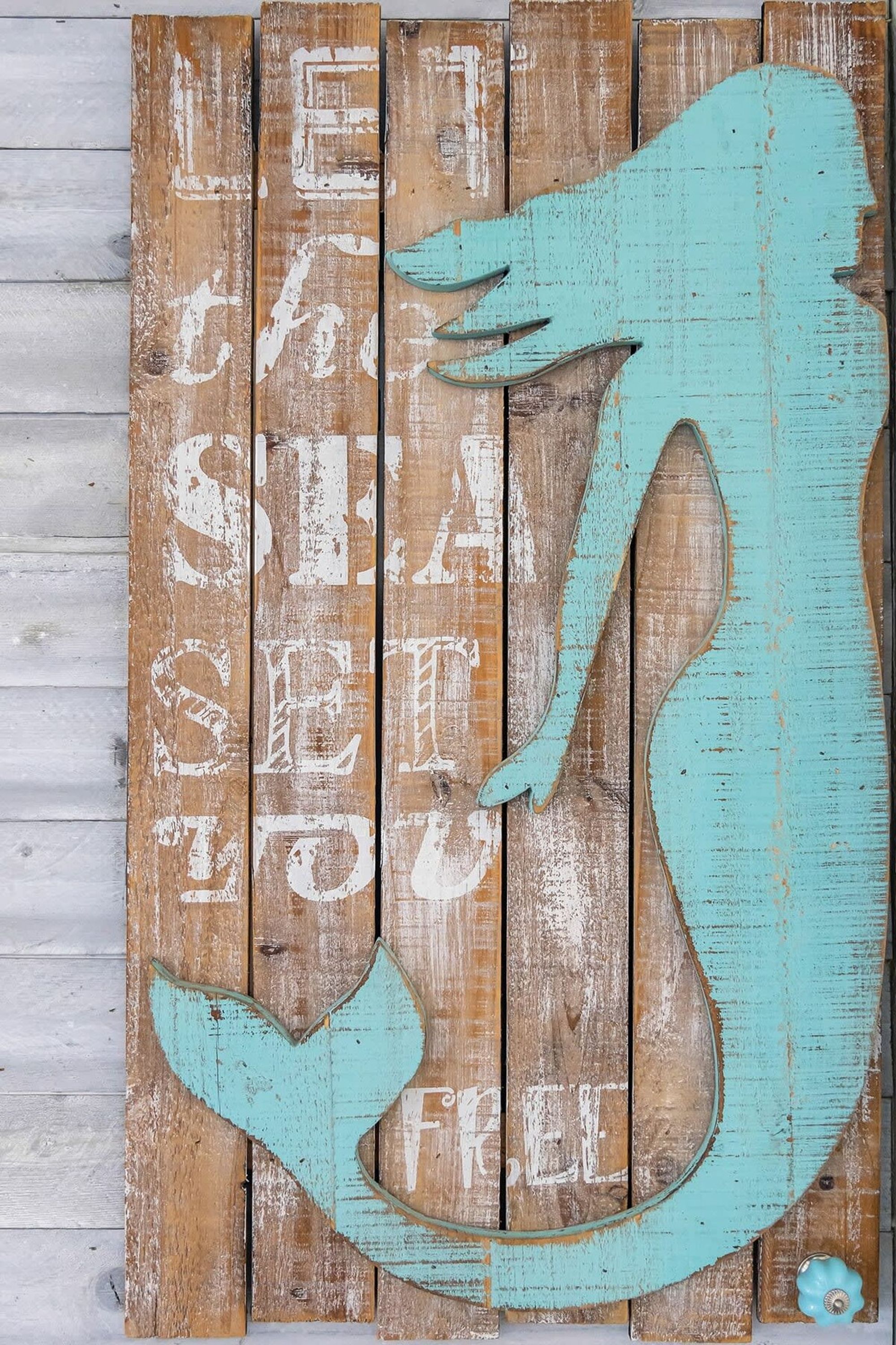 Un mur en bois rustique sur lequel est peinte une silhouette turquoise représentant une personne, ainsi que la phrase « LAISSEZ LES REQUINS ÊTRE LIBRES ».