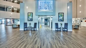 A spacious lobby with a wooden floor, two seating areas with chairs, and a large digital display on the wall.