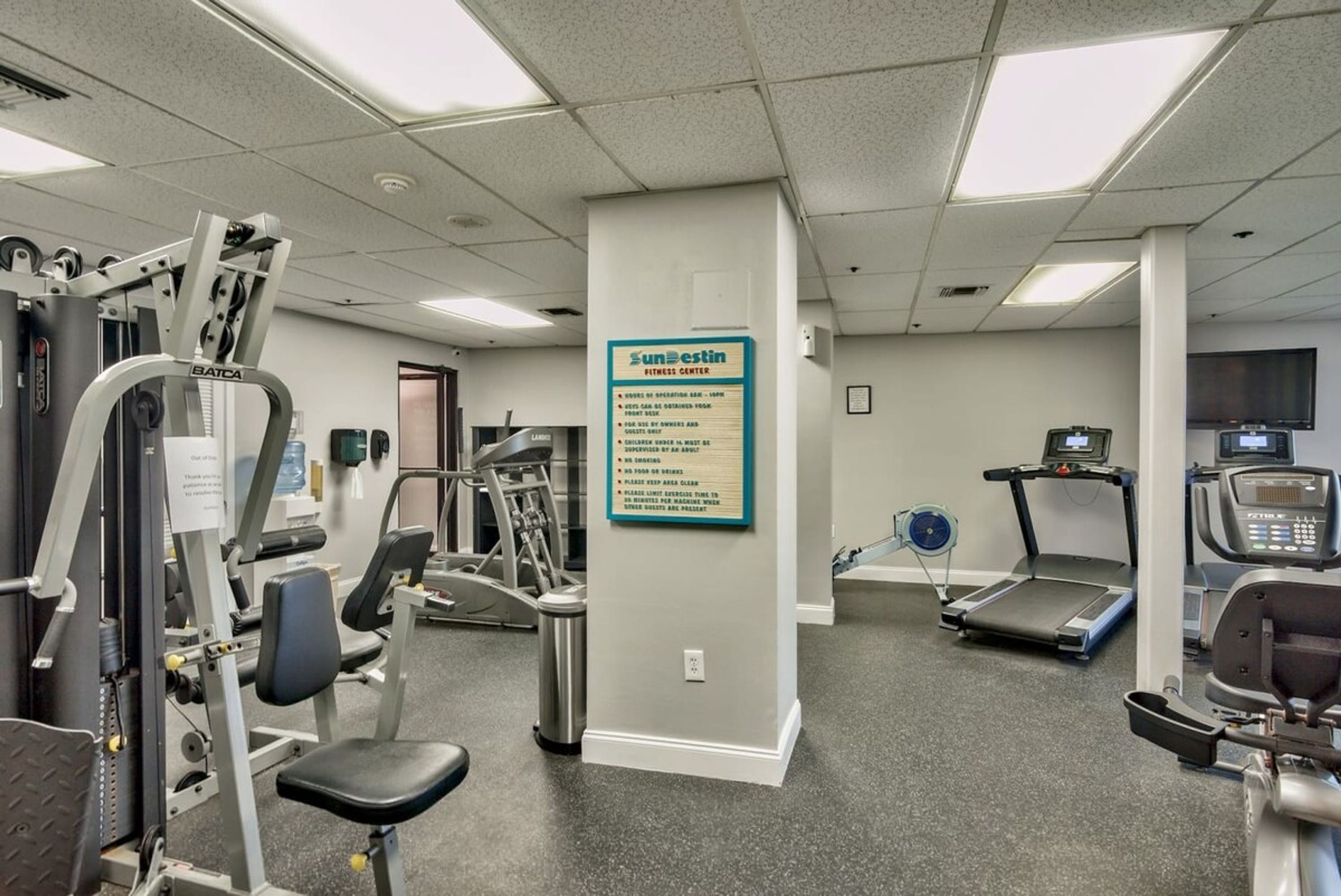 Un centre de remise en forme équipé de divers appareils d’exercice, notamment des tapis de course et des appareils de musculation, et une affiche indiquant le nom du centre et son règlement.