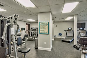 Un gimnasio con diverso equipamiento de ejercicio, incluyendo cintas de correr y máquinas de pesas, y un cartel que muestra el nombre del centro y sus normas.