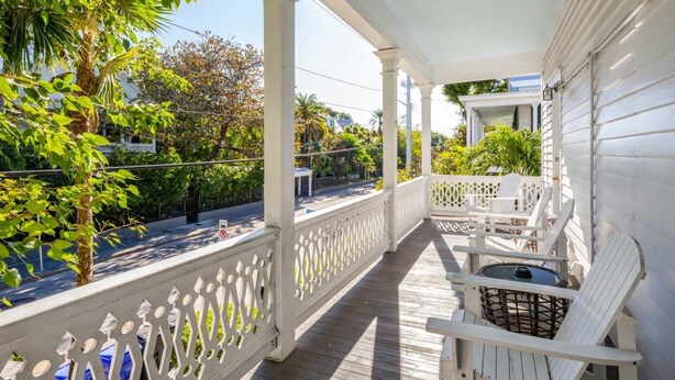 A covered porch with white railings and a view of the street. - Bananas Foster by Brightwild Epic Guesthouse (Key West)