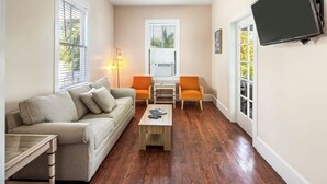 A living room with a sofa, two chairs, a coffee table, and a TV mounted on the wall. - Bananas Foster by Brightwild Epic Guesthouse (Key West)
