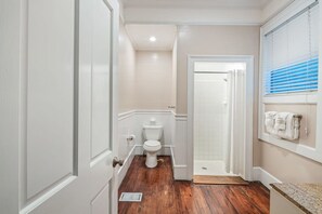 A bathroom with a white toilet, a shower area, and a wooden floor. - Bananas Foster by Brightwild Epic Guesthouse (Key West)