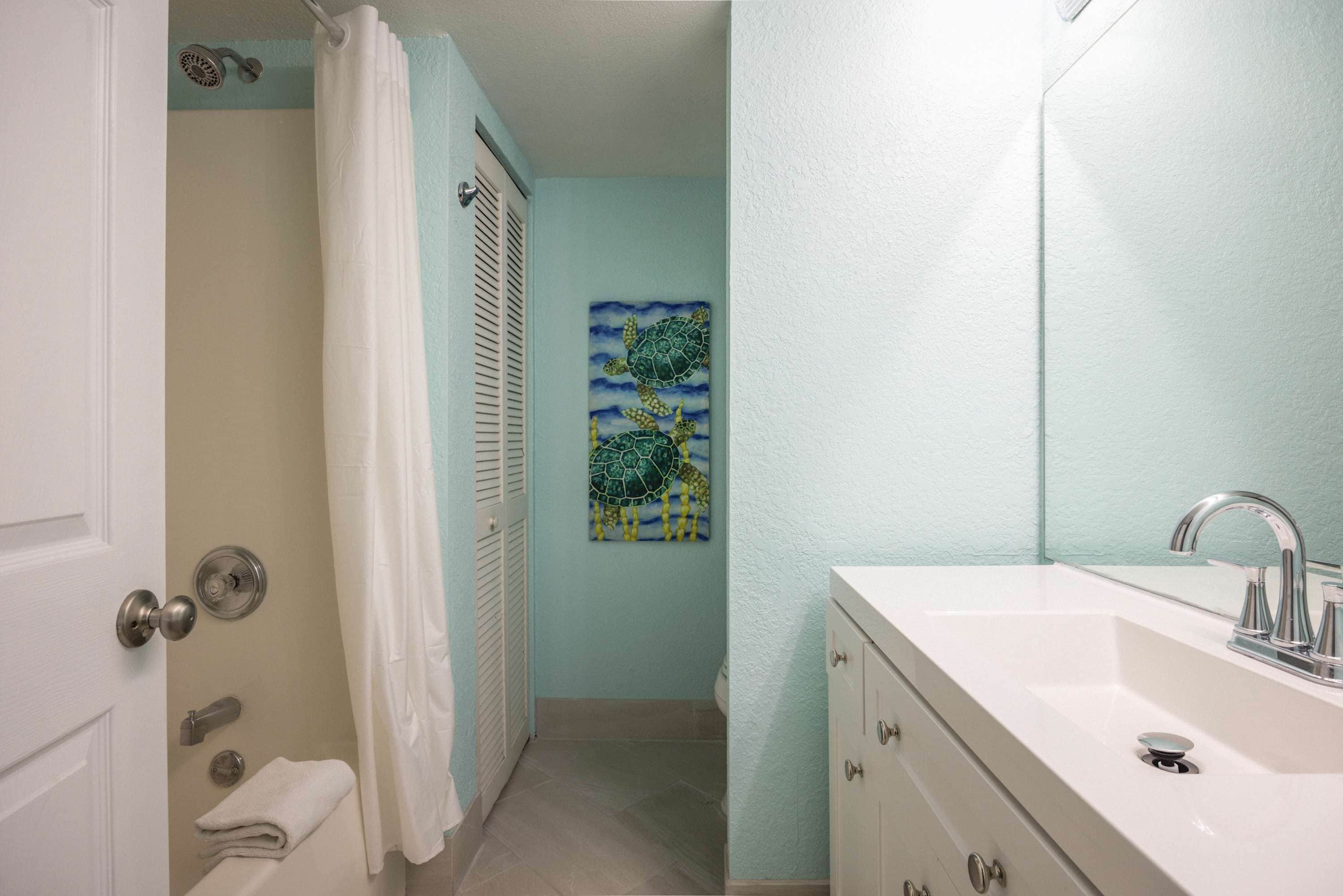 A bathroom with a white sink, a shower curtain, and a towel on the floor.