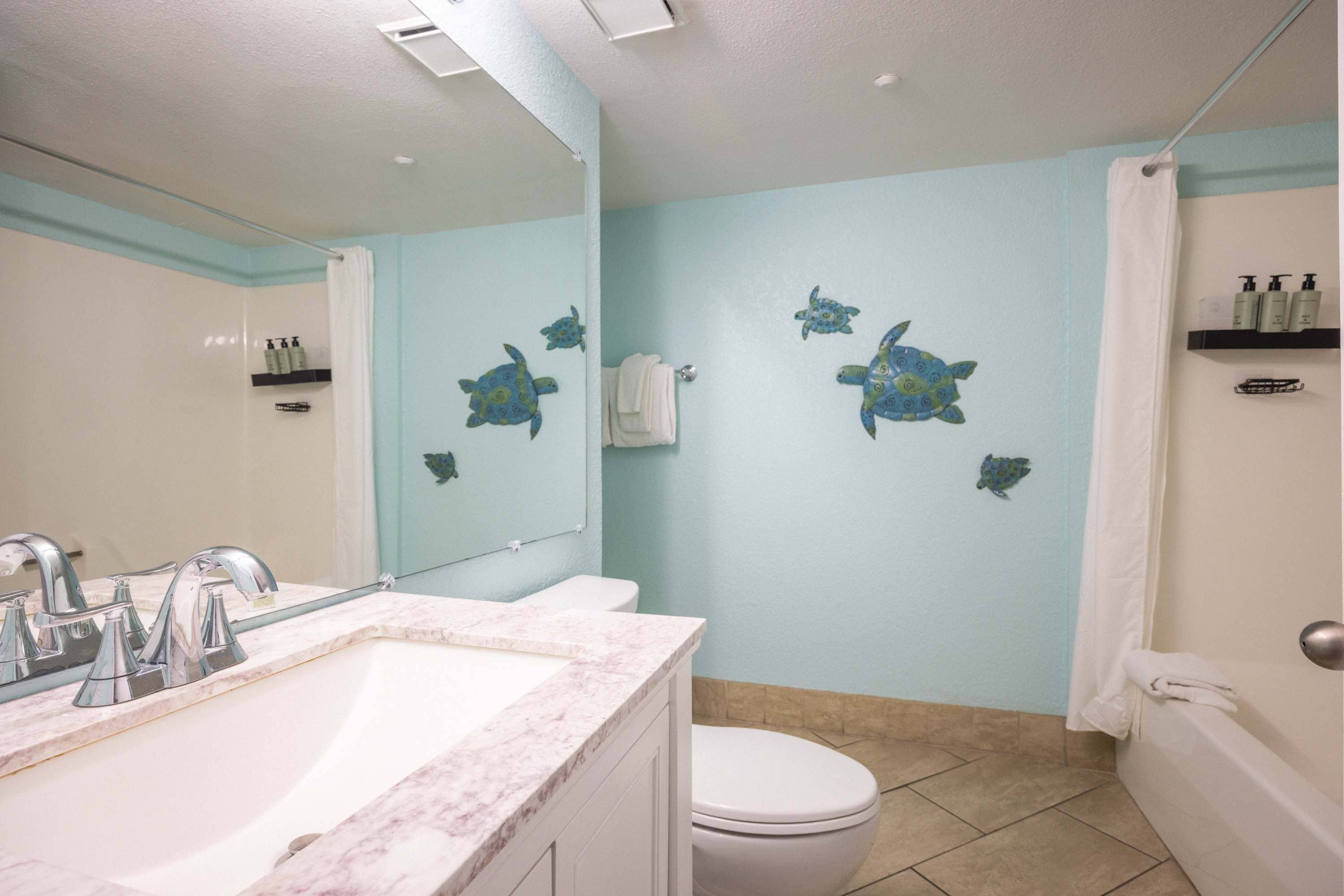 Un baño con lavamanos blanco, inodoro blanco y bañera. Hay calcomanías decorativas de tortugas en la pared.