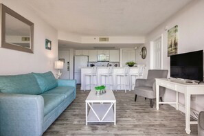A living room with a sofa, a coffee table, a TV, and a kitchen in the background. - Tortuga Suite Sparkling Pool Hot Tub (Key West)