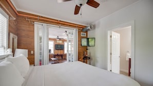 A bedroom with a large bed, wooden walls, a ceiling fan, a TV, and a sliding door leading to a dining area. - Commodore s Compound by Brightwild Huge Home (Key West)