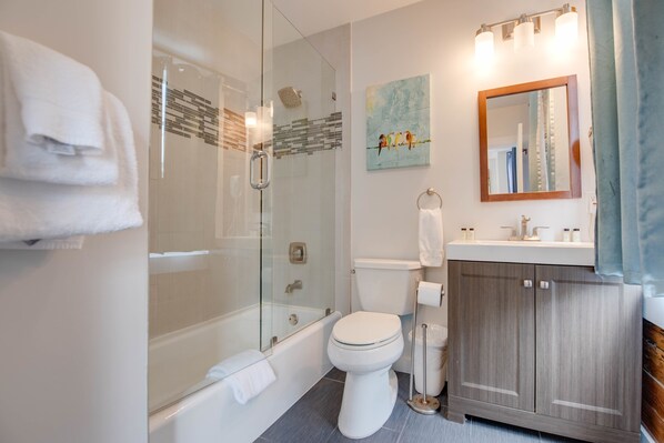 A modern bathroom with a glass-enclosed shower, a white toilet, a wooden vanity, and a painting on the wall. - Commodore s Compound by Brightwild Huge Home (Key West)