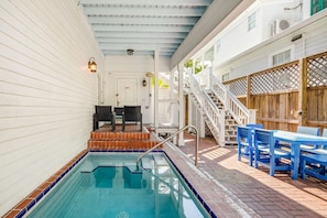 A pool area with a tiled deck, a wooden fence, and a staircase leading to a covered porch. - Sweet Caroline by Brightwild Pool Parking (Key West)