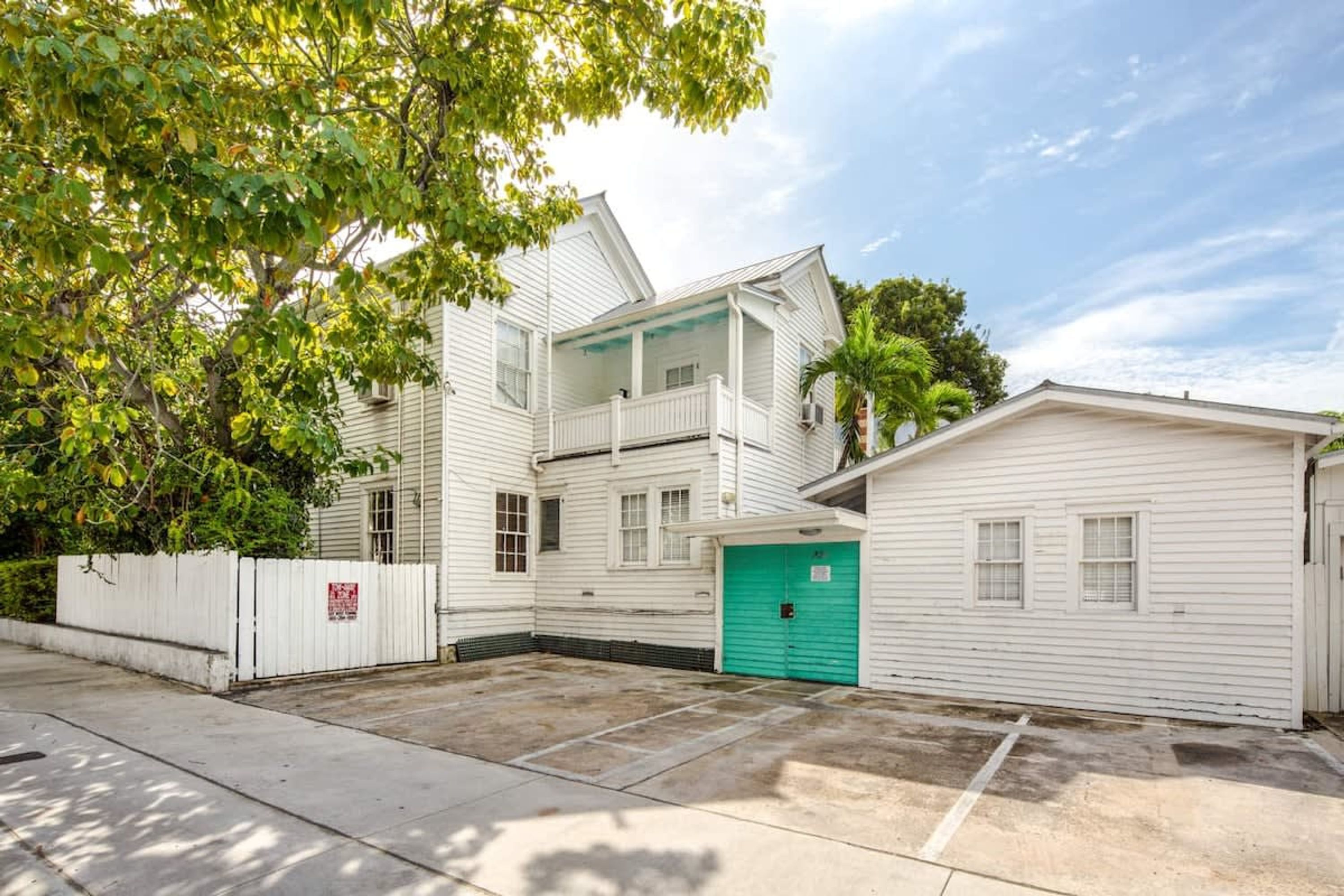 A two-story white building with a green garage door, a covered porch, and a fenced yard.