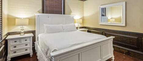 Une chambre à coucher classique, avec un grand lit, deux tables de chevet, une commode, un miroir et une fenêtre avec des stores.