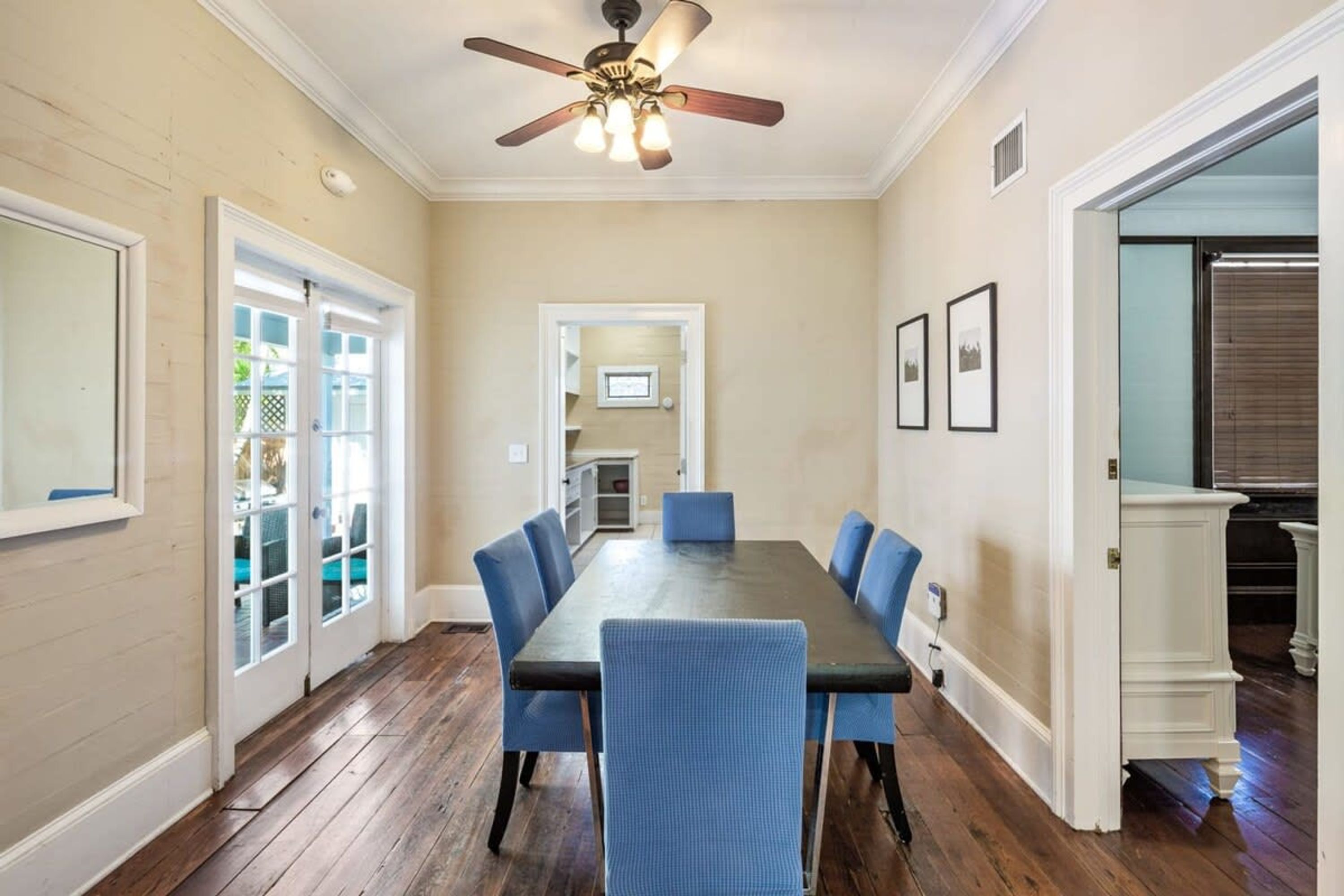 A dining room with a long table, blue chairs, and a ceiling fan.