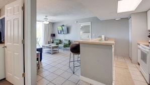 Een moderne keuken met een centraal eiland, een eetgedeelte met tafel en stoelen, en een woonkamer met een bank en een televisie.