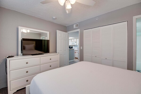 A bedroom with a bed, a dresser, a mirror, a ceiling fan, and a closet.