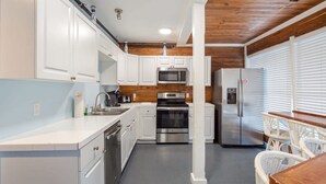 Una cucina moderna con mobili bianchi, elettrodomestici in acciaio inossidabile e un soffitto in legno.