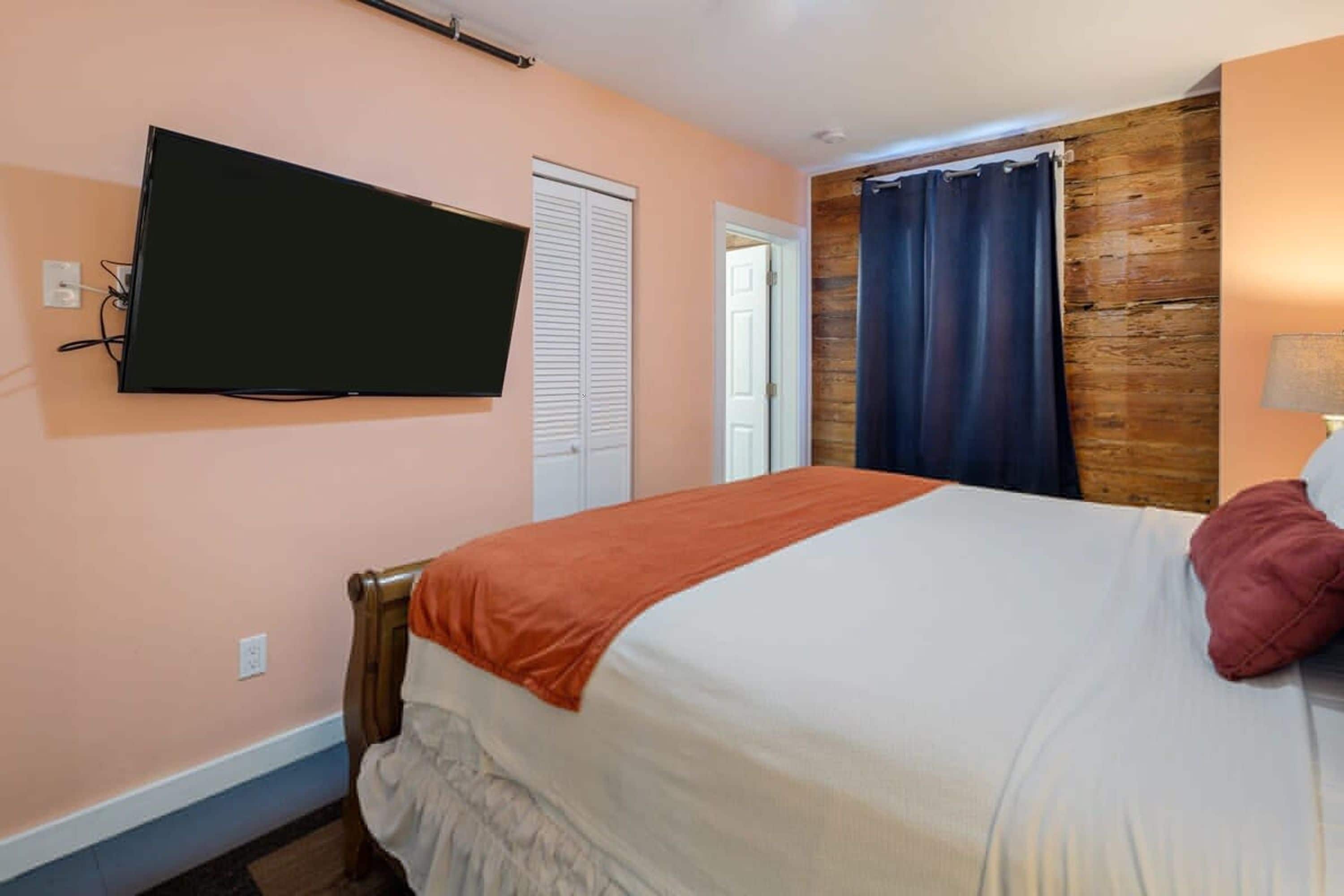 A bedroom with a bed, a television mounted on the wall, a door, and a curtain.