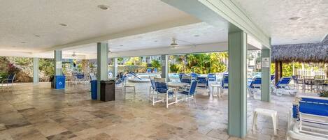 An outdoor pool area with blue and white lounge chairs, a covered seating area, and a thatched-roof structure.