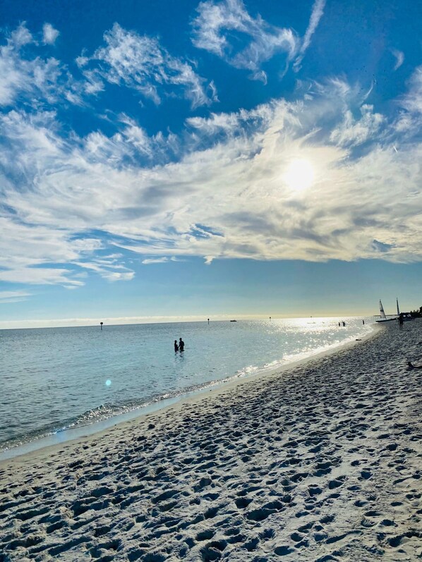 A beach with footprints leading to the water, a clear sky, and a distant sailboat. - Island Time Gorgeous Condo Steps To The Beach (Key West)