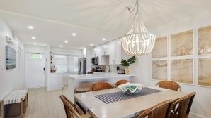 A modern kitchen with white cabinets, a central island, and a chandelier. - Island Time Gorgeous Condo Steps To The Beach (Key West)