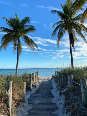 A wooden pathway leading to a beach with palm trees and a clear blue sky. - Island Time Gorgeous Condo Steps To The Beach (Key West)