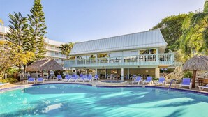A hotel with a swimming pool, lounge chairs, and a thatched-roof structure. - Island Time Gorgeous Condo Steps To The Beach (Key West)