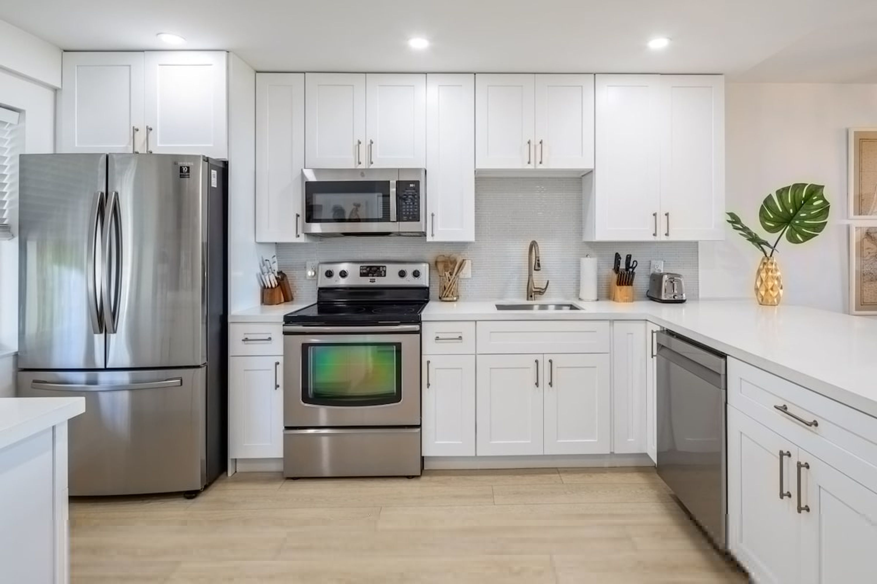 Una cocina moderna con armarios blancos, electrodomésticos de acero inoxidable y piso de madera.